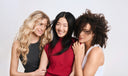 Three women with different hair colors posing together against a plain background